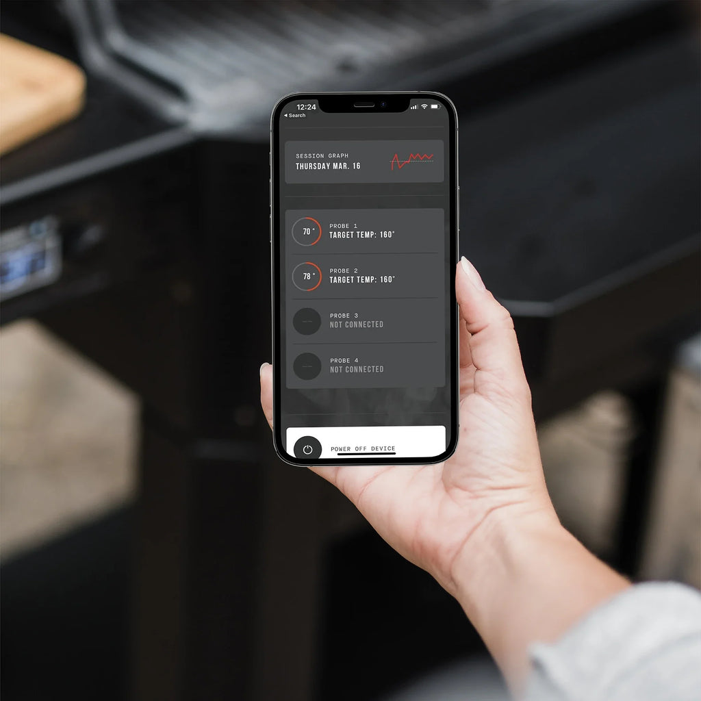 A hand holding a smart phone running the Masterbuilt app. The app shows the cook session temperature graph at the top. Below are information boxes for 4 temperature probes. The top 2 show probe current and target temperatures.