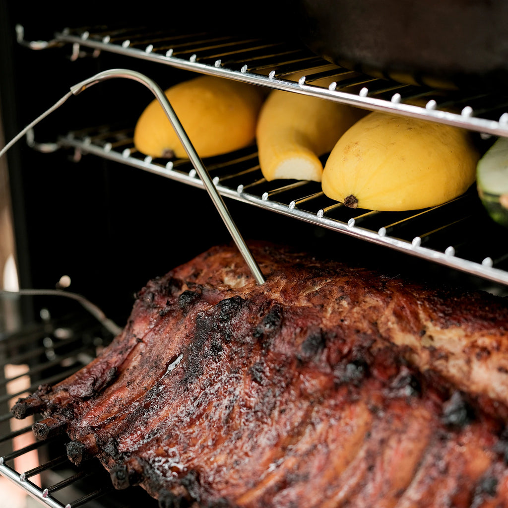 Meat probe shown inserted into a rack of ribs  that is sitting on one of the smoker racks.