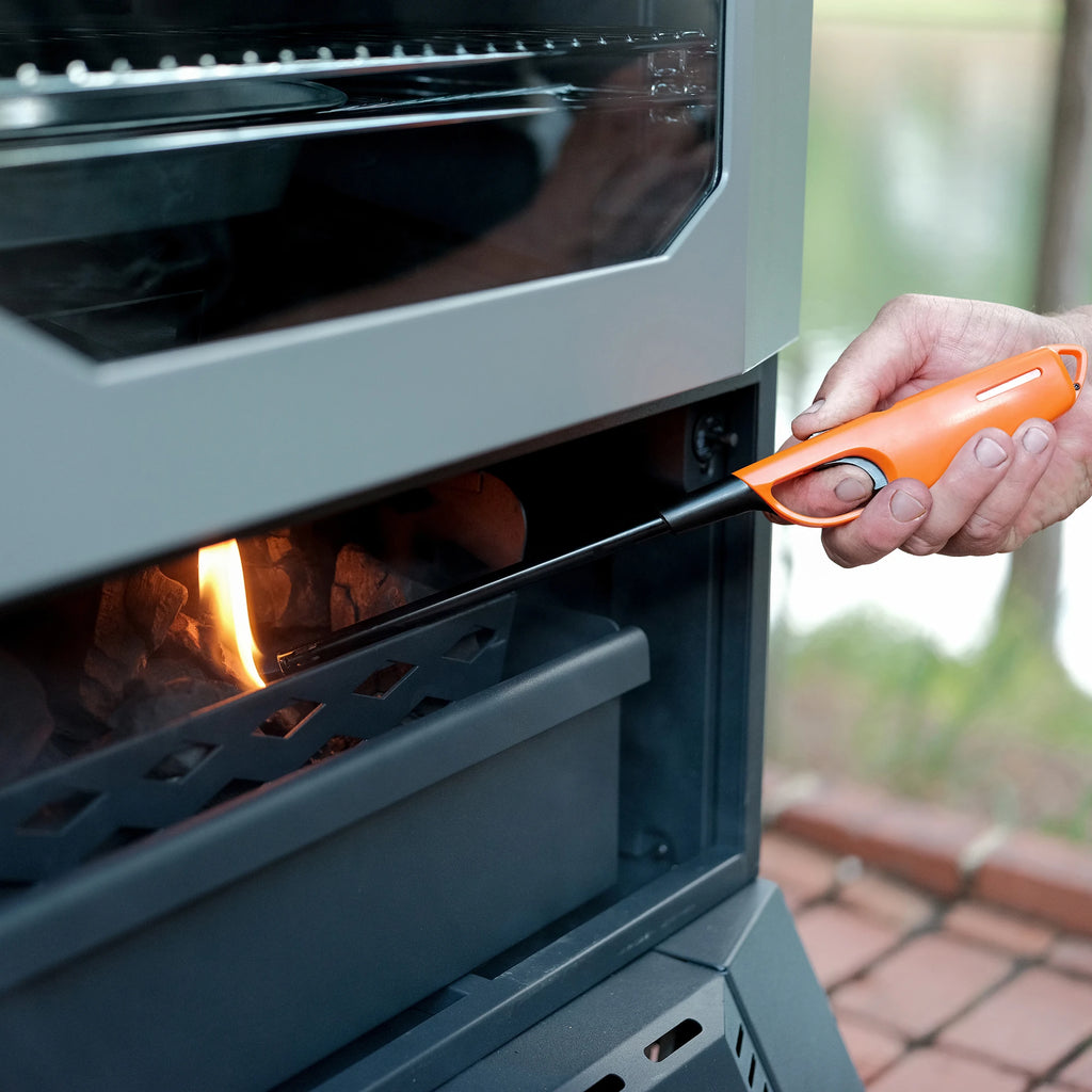 Bottom door of charcoal smoker opens for easy access to the firebox. Shown here as a person lights charcoal in the hopper while main smoker door is closed.