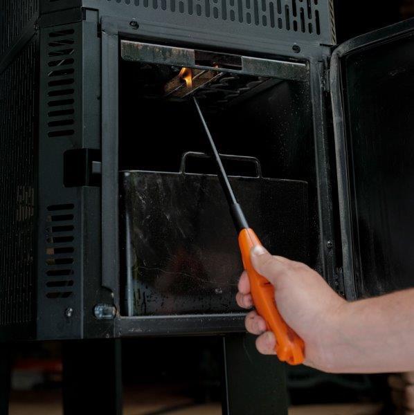 A person uses a long lighter to ignite the fire at the bottom of the hopper, reached through an access door on the side