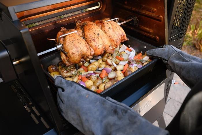 Chickens on the rotisserie over a tray of mixed vegetables
