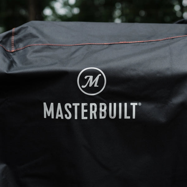 The Masterbuilt name and logo printed in white on the black grill cover. Several of the seams, double-stitched with orange thread, are visible.