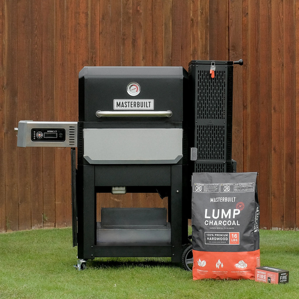Masterbuilt Gravity Series bbq with a bag of lumpwood charcoal on grass against a wooden fence.
