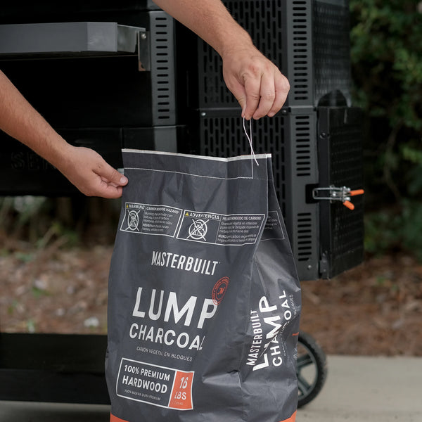 Person opening a bag of Masterbuilt lump charcoal in front of a grill.