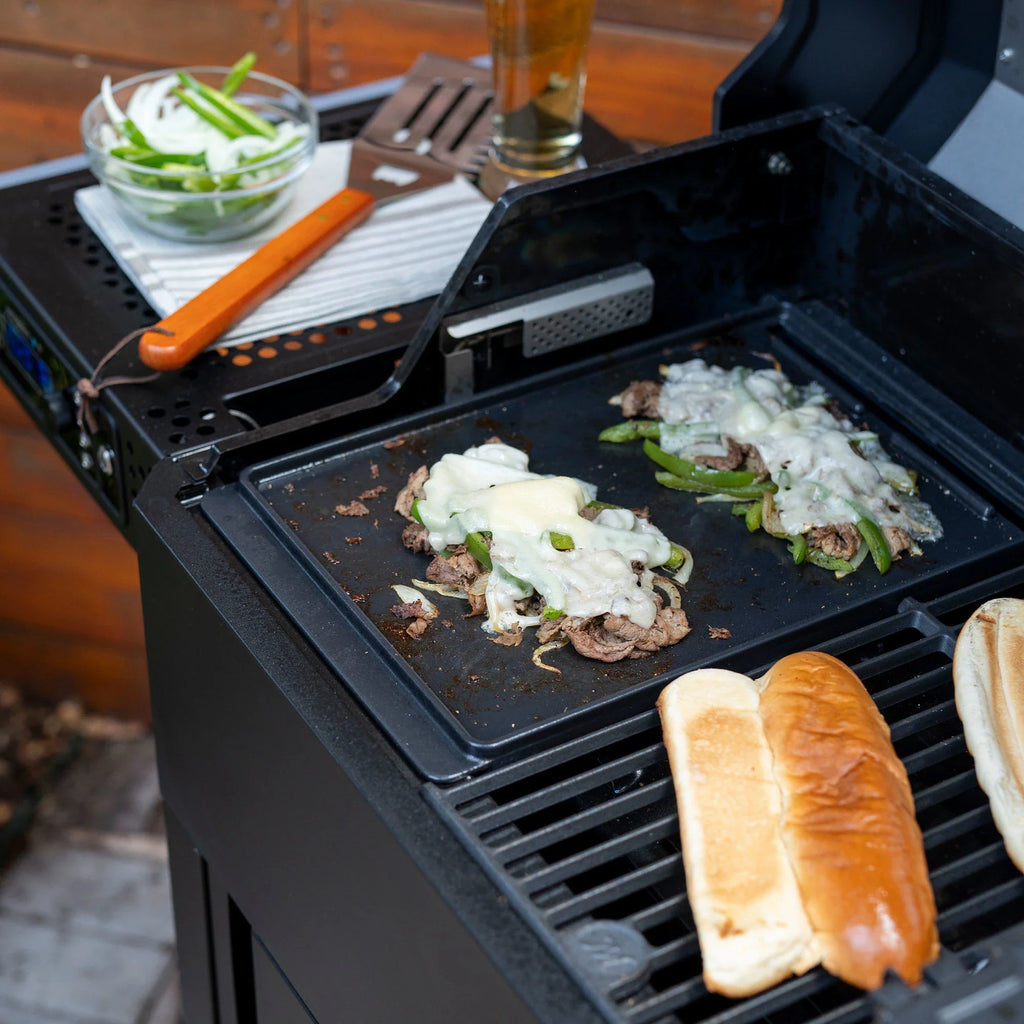 Cooking Philly cheesesteaks on a griddle installed flat side up in an AutoIgnite grill. The griddle takes up half the cooking space, while a regular cooking grate fills the other half of the cooking space and is used for toasting hoagie rolls.