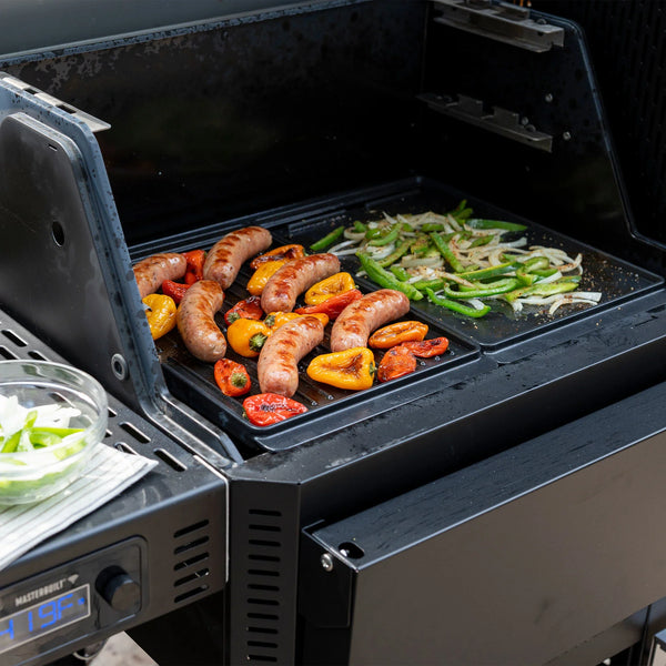 2 griddles installed in a Gravity Series grill. The left is ribbed-side up and has sausages and whole peppers searing on it. The right side is flat side up for cooking strips of onion and bell pepper.