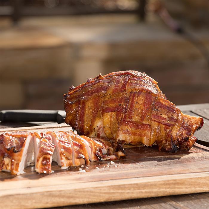 Pork loin wrapped in bacon and smoked rests on a cutting board ready for serving